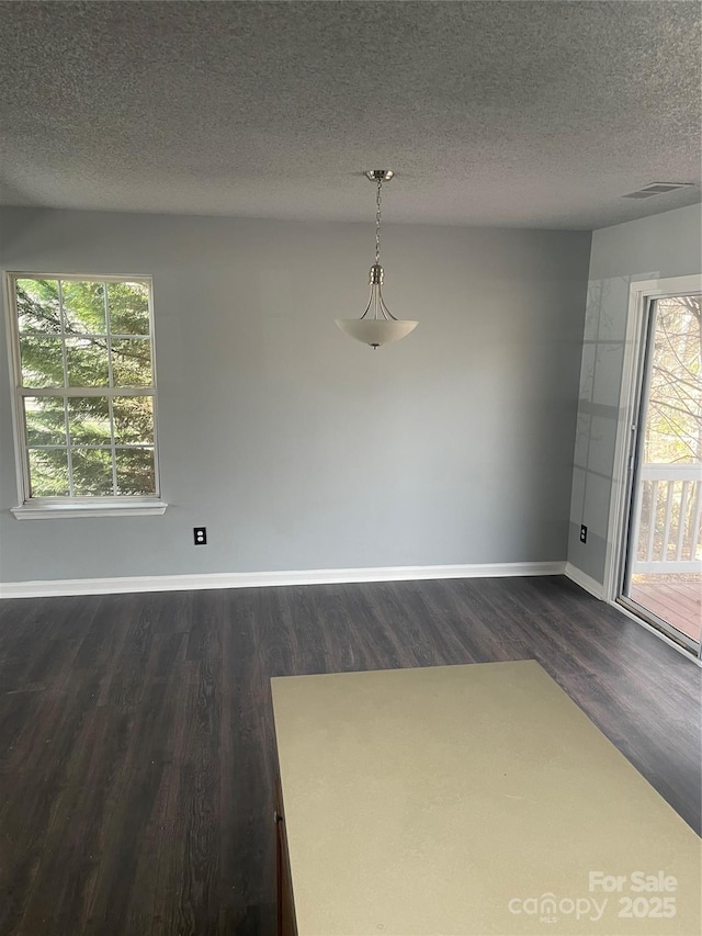 unfurnished dining area featuring dark wood-style floors, baseboards, visible vents, and a textured ceiling