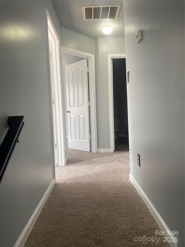 hall with a textured ceiling, carpet flooring, visible vents, and baseboards