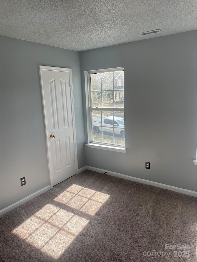 spare room featuring light carpet, a textured ceiling, visible vents, and baseboards