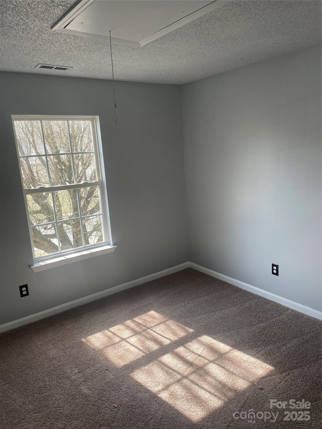 carpeted spare room featuring a textured ceiling, visible vents, attic access, and baseboards