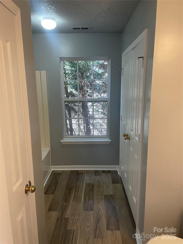 interior space featuring dark wood-style flooring, visible vents, a textured ceiling, and baseboards