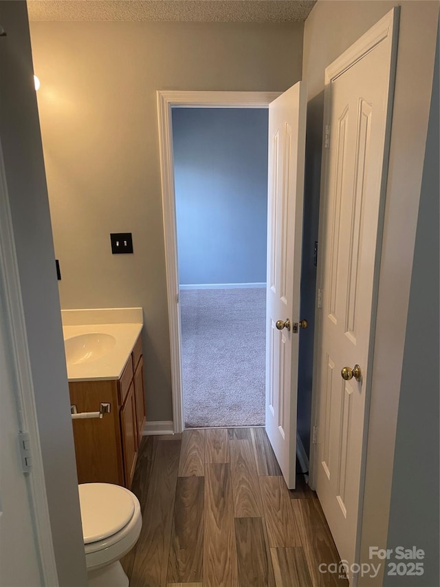 bathroom featuring toilet, a textured ceiling, vanity, wood finished floors, and baseboards