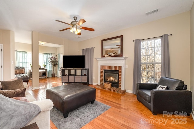 living room featuring a brick fireplace, light hardwood / wood-style floors, and a healthy amount of sunlight