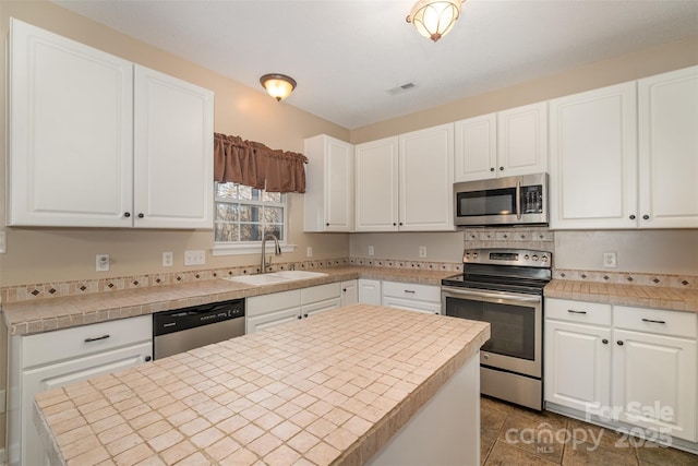 kitchen with sink, white cabinetry, a center island, tile counters, and stainless steel appliances