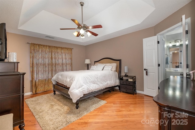 bedroom with a tray ceiling, wood-type flooring, and ceiling fan