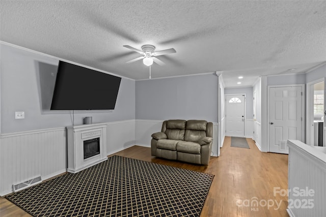 living room featuring crown molding, ceiling fan, a textured ceiling, and light wood-type flooring