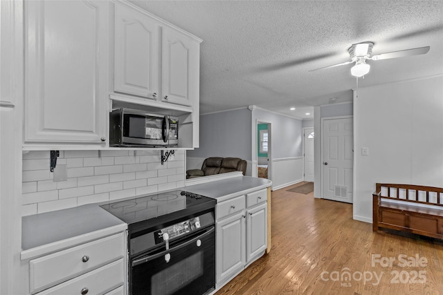 kitchen with black electric range oven, light wood-type flooring, backsplash, white cabinets, and a textured ceiling