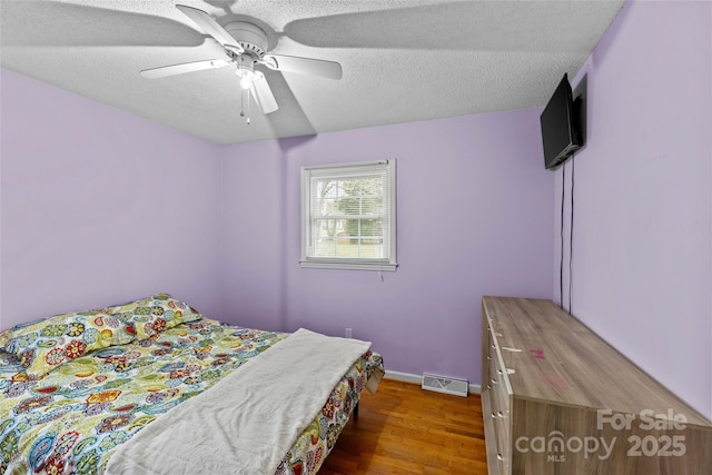 bedroom with ceiling fan, hardwood / wood-style flooring, and a textured ceiling