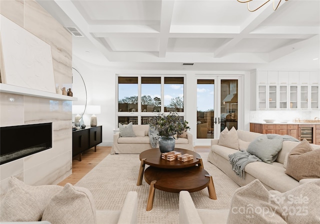 living room with coffered ceiling, beverage cooler, beamed ceiling, a fireplace, and light hardwood / wood-style floors