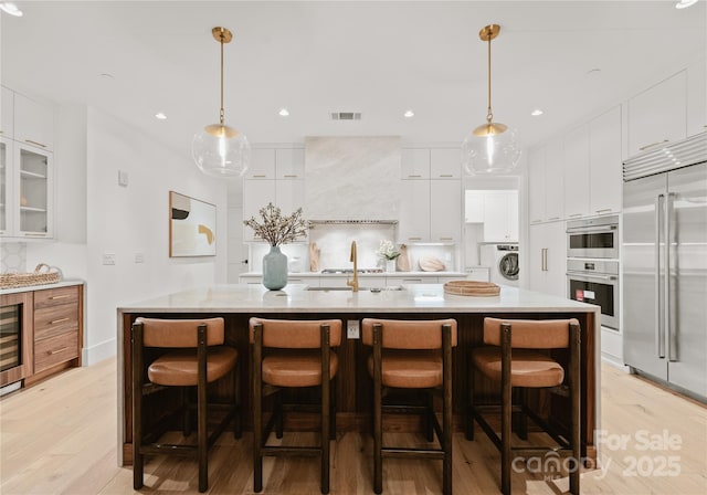 kitchen featuring appliances with stainless steel finishes, washer / dryer, white cabinets, decorative light fixtures, and a large island with sink