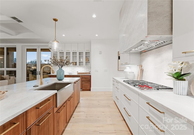 kitchen featuring premium range hood, sink, tasteful backsplash, stainless steel gas stovetop, and white cabinets