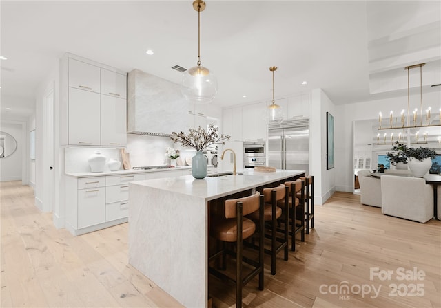 kitchen featuring gas stovetop, a center island with sink, white cabinets, decorative backsplash, and wall chimney range hood