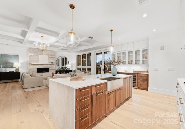 kitchen with a kitchen island with sink, sink, coffered ceiling, and white cabinets