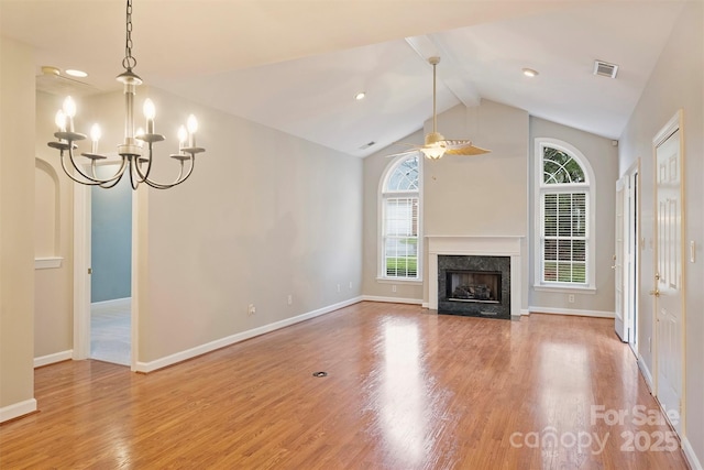 unfurnished living room featuring lofted ceiling with beams, wood-type flooring, a premium fireplace, and ceiling fan with notable chandelier