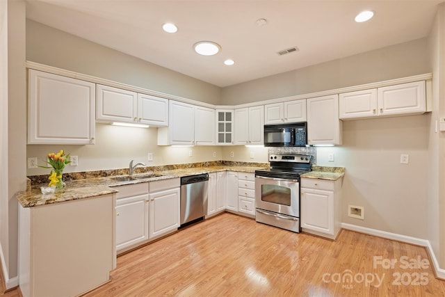 kitchen with stone counters, appliances with stainless steel finishes, sink, white cabinets, and light hardwood / wood-style flooring