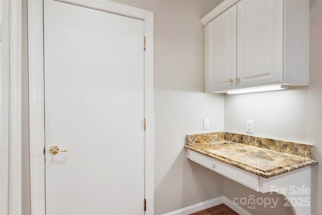 kitchen featuring light stone counters, built in desk, and white cabinets