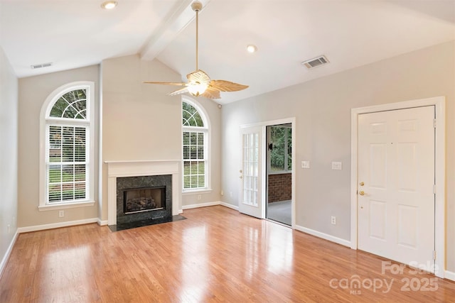 unfurnished living room with lofted ceiling with beams, a wealth of natural light, a fireplace, and light wood-type flooring