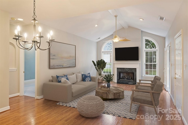 living room with ceiling fan with notable chandelier, vaulted ceiling with beams, hardwood / wood-style floors, and a fireplace