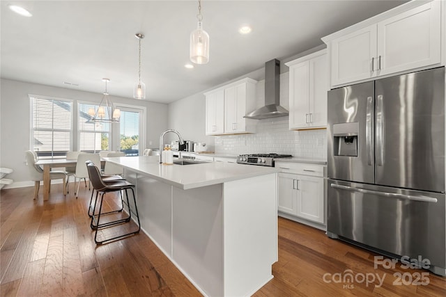 kitchen featuring sink, stainless steel refrigerator with ice dispenser, white cabinets, a center island with sink, and wall chimney exhaust hood