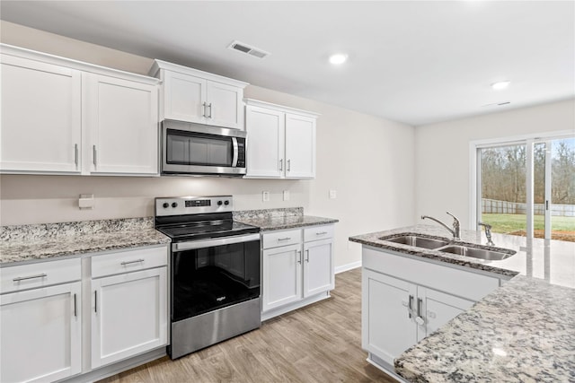 kitchen with appliances with stainless steel finishes, sink, white cabinets, light stone counters, and light hardwood / wood-style floors