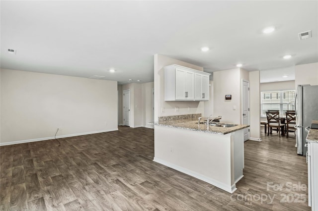 kitchen with sink, stainless steel refrigerator, light stone countertops, white cabinets, and dark hardwood / wood-style flooring