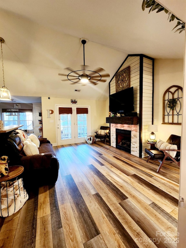 living room with ceiling fan, lofted ceiling, a stone fireplace, and hardwood / wood-style floors