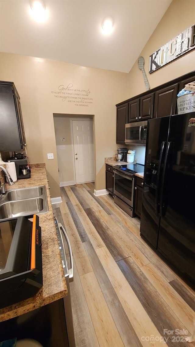 kitchen with sink, stainless steel appliances, light stone countertops, vaulted ceiling, and light wood-type flooring