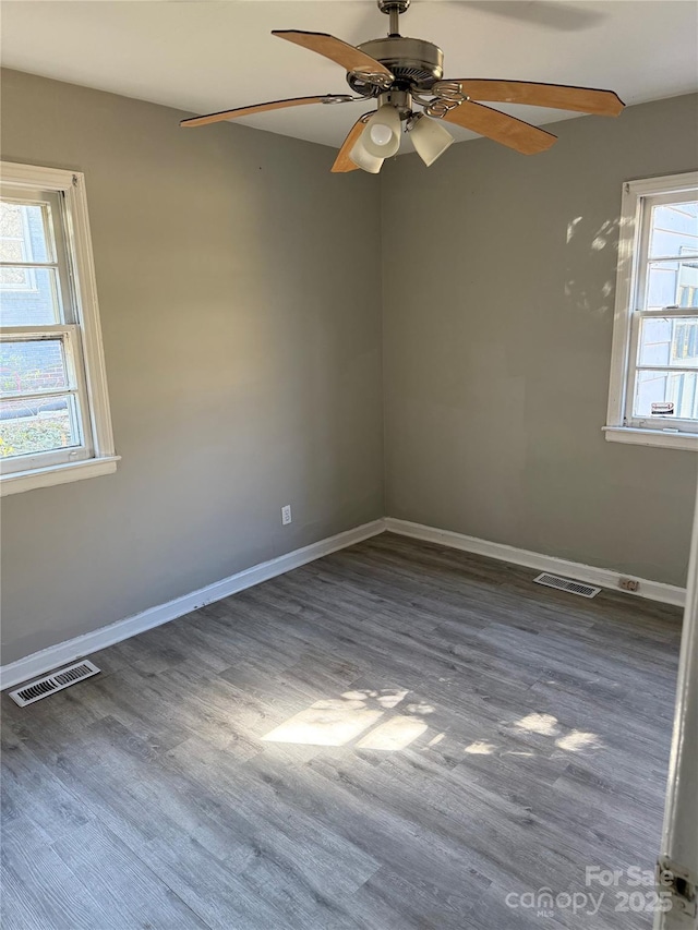 empty room featuring plenty of natural light, dark wood-type flooring, and ceiling fan