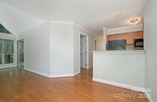 kitchen featuring lofted ceiling, crown molding, light hardwood / wood-style flooring, fridge, and decorative backsplash