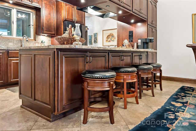 bar with black fridge, light stone countertops, and decorative backsplash