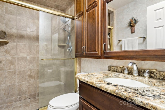 bathroom featuring a shower with door, vanity, and toilet