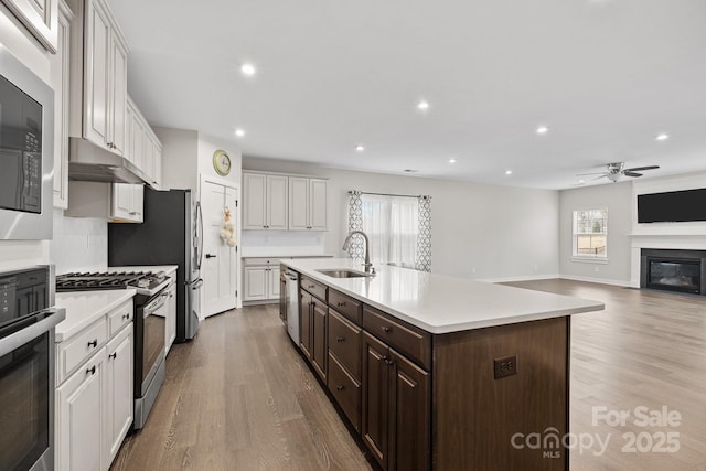 kitchen featuring an island with sink, white cabinetry, sink, stainless steel appliances, and dark brown cabinets