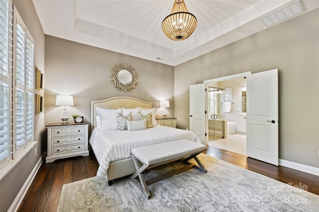 bedroom with dark hardwood / wood-style flooring, connected bathroom, a tray ceiling, and an inviting chandelier