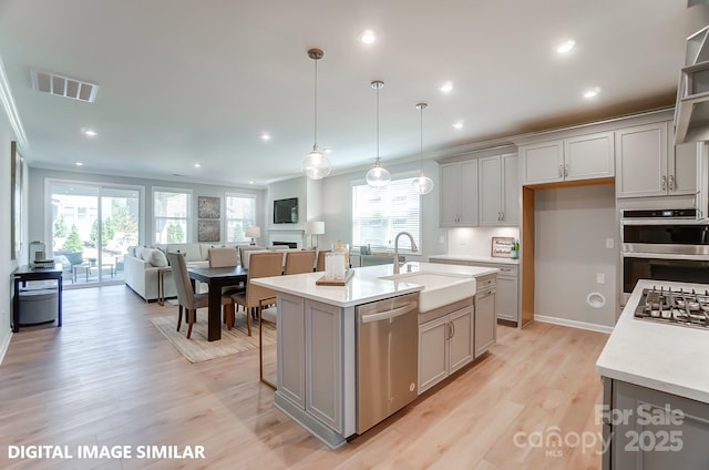 kitchen featuring appliances with stainless steel finishes, sink, hanging light fixtures, a kitchen island with sink, and crown molding