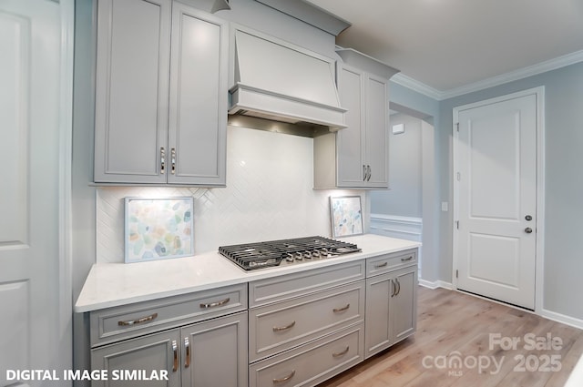 kitchen featuring light hardwood / wood-style flooring, premium range hood, tasteful backsplash, ornamental molding, and stainless steel gas cooktop