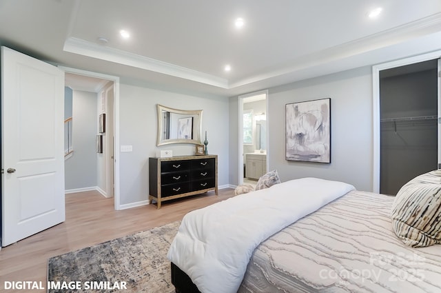 bedroom with ensuite bath, wood-type flooring, a spacious closet, a raised ceiling, and a closet