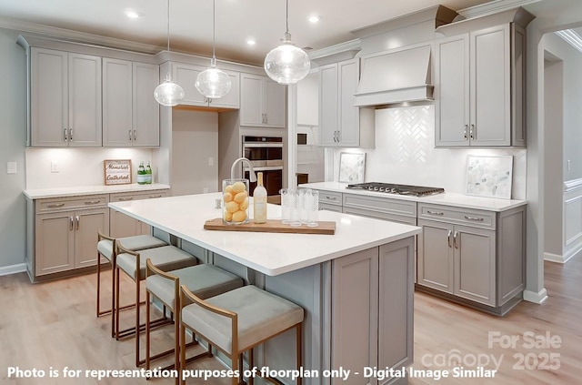 kitchen with a center island with sink, stainless steel appliances, gray cabinetry, light countertops, and a kitchen bar