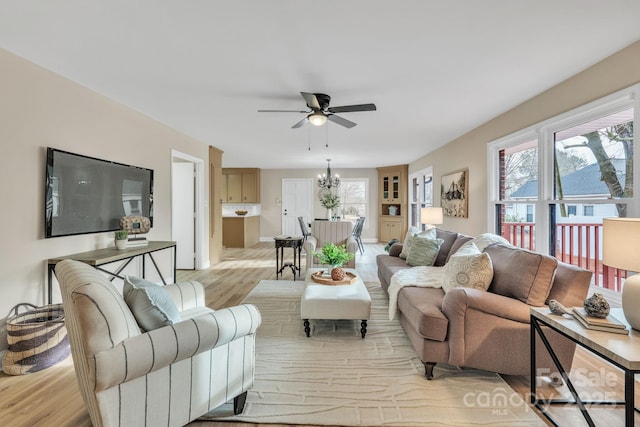 living room with ceiling fan with notable chandelier, built in features, and light hardwood / wood-style flooring