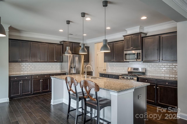 kitchen with sink, appliances with stainless steel finishes, a kitchen island with sink, hanging light fixtures, and light stone countertops