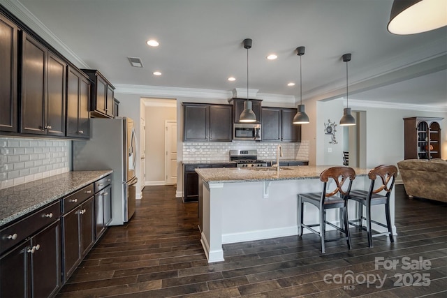 kitchen with appliances with stainless steel finishes, a breakfast bar, hanging light fixtures, dark brown cabinetry, and light stone countertops