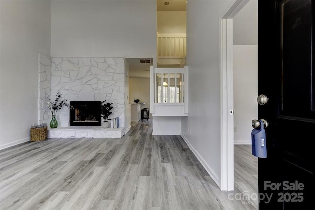 unfurnished living room featuring a towering ceiling, a fireplace, and light hardwood / wood-style floors