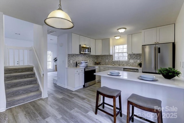 kitchen with hanging light fixtures, appliances with stainless steel finishes, sink, and white cabinets