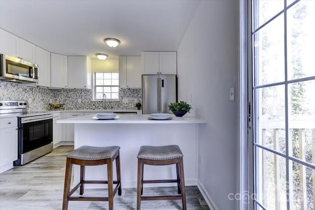 kitchen featuring a kitchen bar, sink, white cabinetry, stainless steel appliances, and decorative backsplash