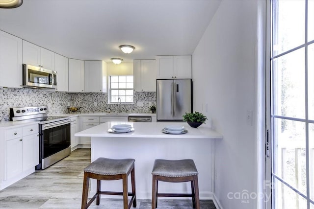 kitchen with appliances with stainless steel finishes, tasteful backsplash, sink, white cabinets, and a kitchen breakfast bar