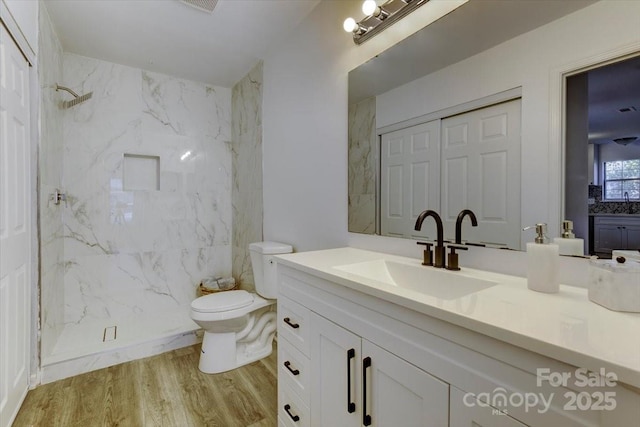 bathroom with wood-type flooring, tiled shower, vanity, and toilet