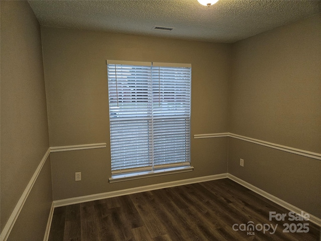 spare room with a textured ceiling and dark hardwood / wood-style flooring