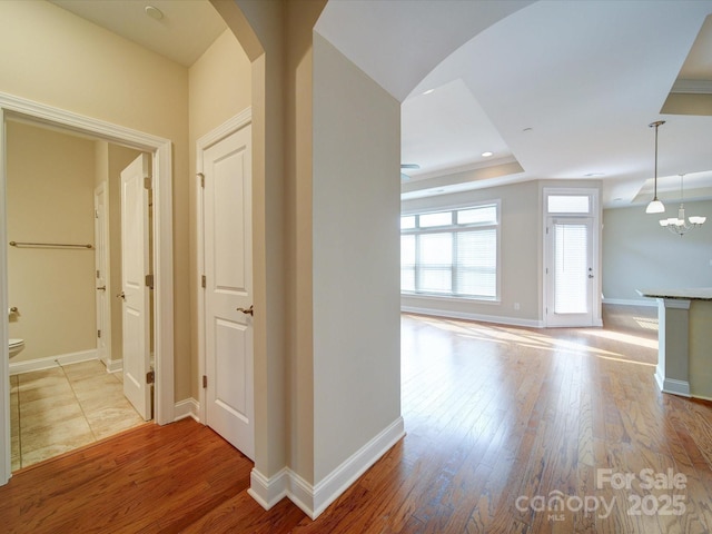 hallway with an inviting chandelier, light wood-type flooring, and a tray ceiling