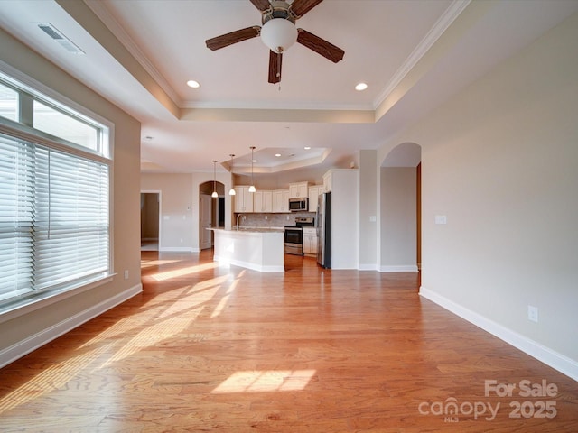 unfurnished living room with a raised ceiling, ornamental molding, ceiling fan, and light wood-type flooring