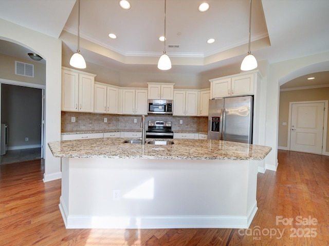 kitchen with pendant lighting, a center island with sink, a raised ceiling, and appliances with stainless steel finishes