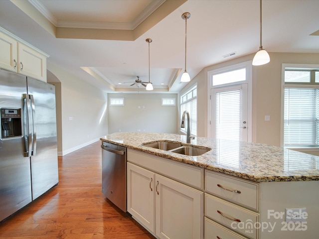 kitchen featuring sink, hanging light fixtures, a tray ceiling, stainless steel appliances, and a kitchen island with sink